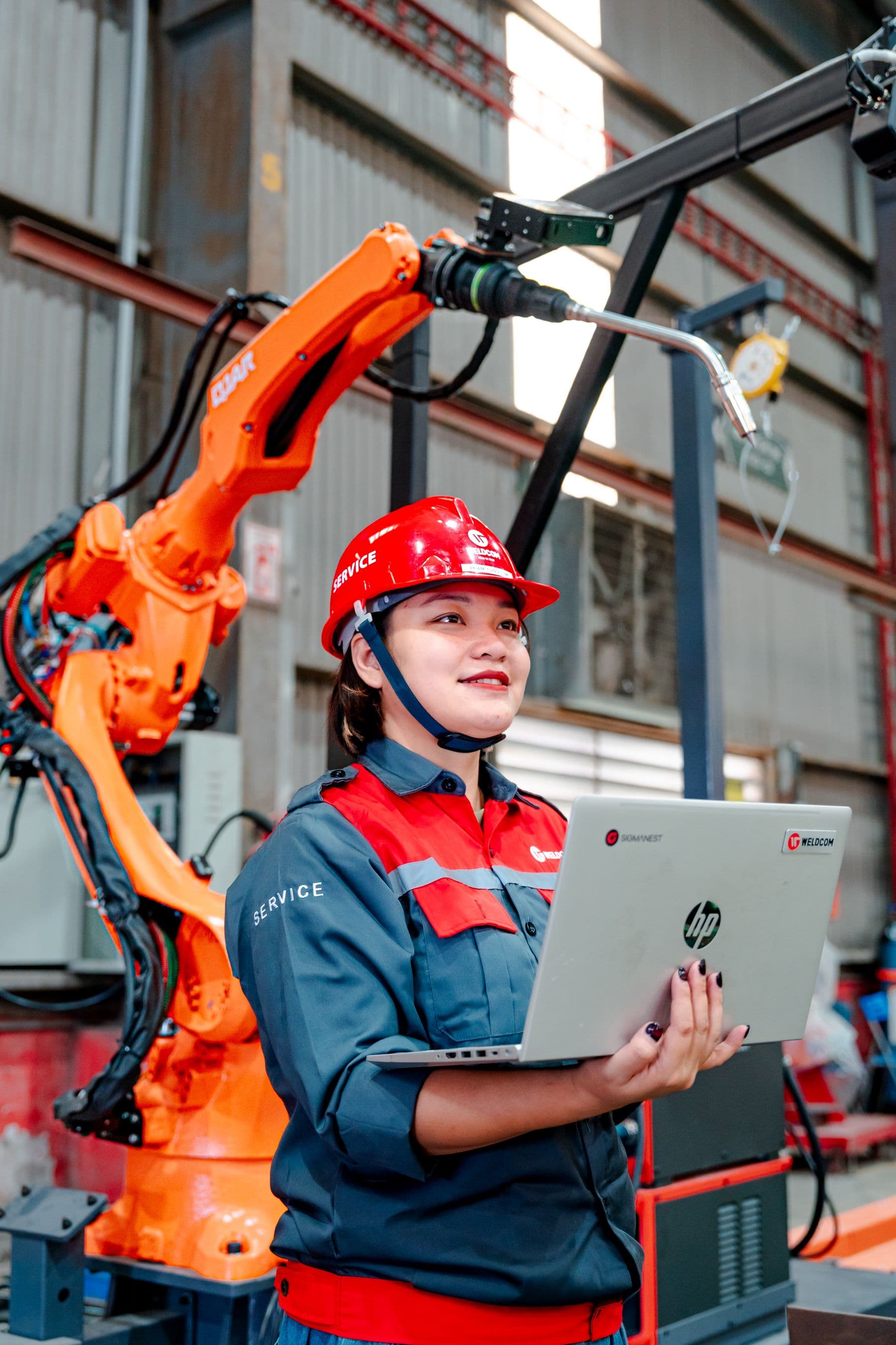 Engineer with laptop overseeing robotic machinery in a factory